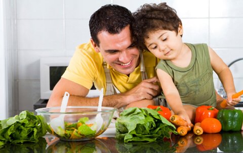 A father shows his son how to prepare salad