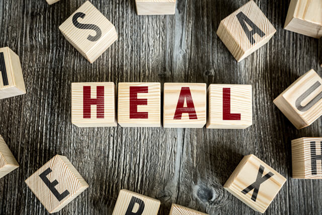 Block letters spell out "heal" on a wooden background