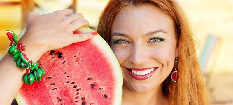 A woman rests a halved watermelon against her shoulder