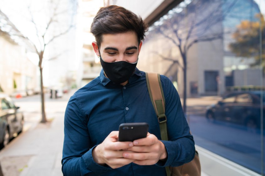 Man wearing COVID mask and on cell phone while walking in a city - Fruit-Powered